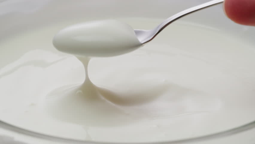 White creamy sauce texture close-up. Dip a spoon into white yogurt macro. Dairy products concept. 