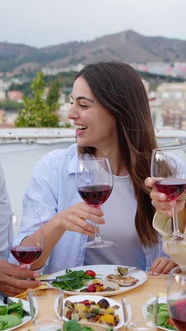 Young beautiful woman toasting red wine with friends on dinner summer party during sunset at home terrace