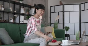 one mature japanese woman open box presents and read card while on video call at home sit on sofa bed