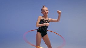 Happy little girl artistic ballerina female gymnast young sport kid child teenager spinning hoop carefree laughing dance spin acrobatic gymnastic exercise have fun rhythmic gymnastics blue background - Powered by Shutterstock - Get 15% off with code: PIKWIZARD15