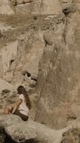 Vertical video. The woman is sitting high on ancient stones in the desert.