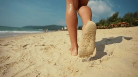 Woman feet barefoot on beach close up. Female tourist walking on the beach by sea ocean, enjoying the sunrise. Close up of legs and feet in the sea water. Travel and tourism, warm journey concept.