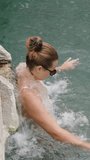 Vertical video. Side View, A Young Woman Bathes in Hot Springs and Stands Under a Water Stream in Cleopatra's Pool in Pamukkale.