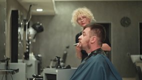 A barber cuts a man's beard with a machine in a barbershop. Businessman in a hairdresser sitting on a chair in front of a mirror, lifestyle care for appearance. High quality 4k footage - Powered by Shutterstock - Get 15% off with code: PIKWIZARD15