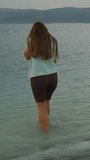 Vertical video. Desolate Mountain Lake, storm clouds in the sky, a young woman dips her feet into the water.