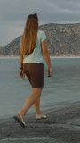 Vertical video. Stormy Clouds over the Lake amidst the Mountains. A Woman walks along the deserted Shore.