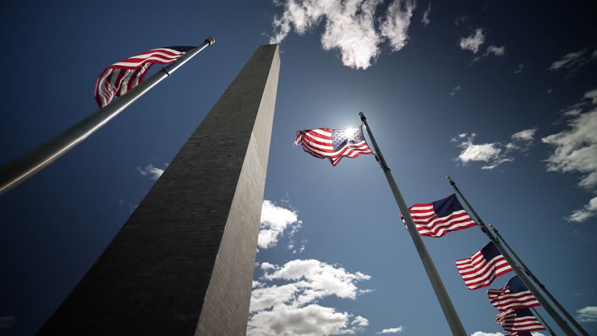 American flags waving in the wind at the Washington Monument with the sun shining in Washington, DC.