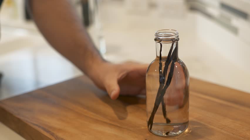 Man closes glass bottle with vanilla beans and vodka to make homemade vanilla.