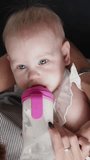 Young mother feeding baby drinking from milk bottle. Vertical video.