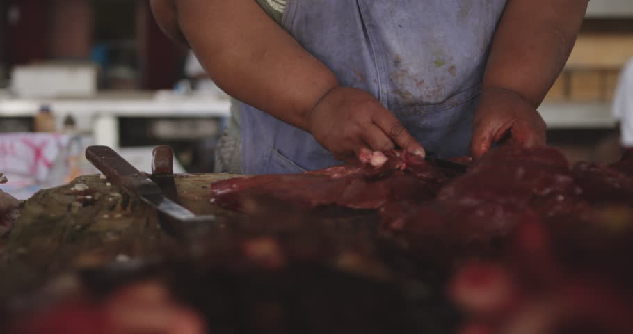 Front view of an African female butcher wearing a headscarf in a township workshop, cutting fresh meat with knife, slow motion
