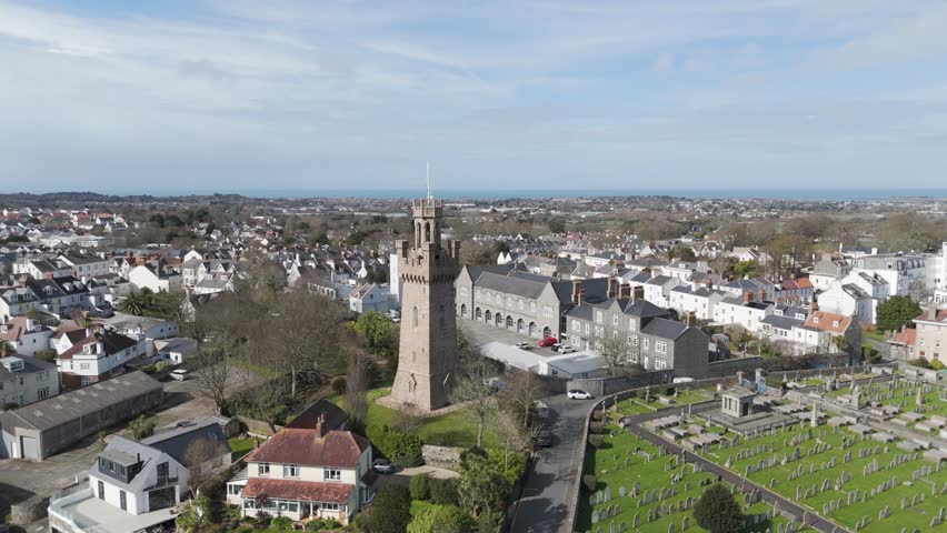Flight over Fire Station,Arsenal and cemetery St Peter Port,Guernsey on bright day close to tower. Royalty-Free Stock Footage #3478112605