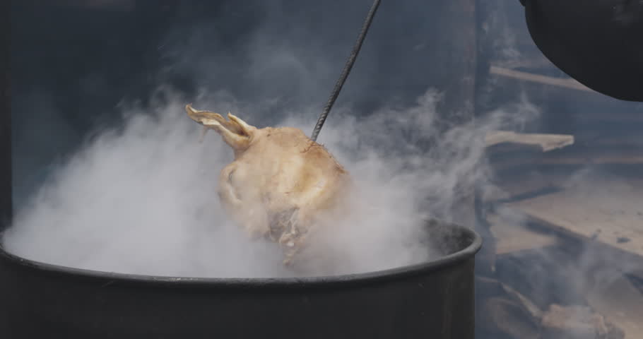 Front view mid section of an African male butcher in a township workshop, picking an animal head with a stake and putting it in bucket, slow motion