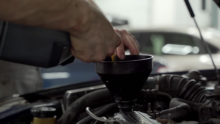 Auto mechanic performs oil change, funnel guides fresh lubricant into engine, hands engage in vehicle maintenance, replacing filters and fluids in auto repair shop, ensuring car performance.