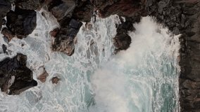 Aerial side view of giant ocean waves crashing and foaming on Shore of Tenerife island with big rock stones. Meeting deep blue ocean water. Vertical video. Slow motion