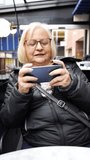 vertical grandma gamer playing video game on smartphone in a cafe in winter