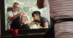 Alternative cool hair salon. Front view of a Caucasian male hairdresser working in a hair salon, tying up hair of a Caucasian female with hair clips in slow motion