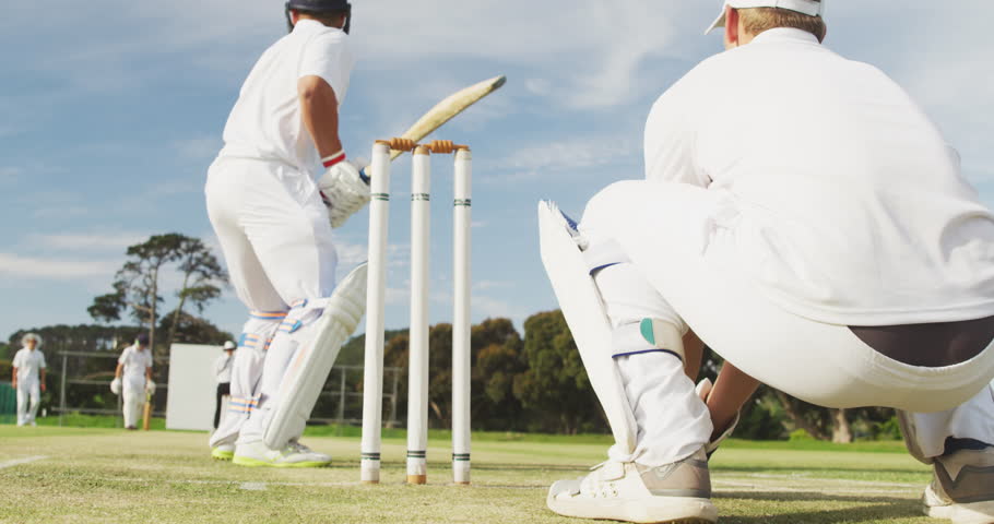 Rear view of a teenage Caucasian male wicket keeper and batsman on the pitch wearing helmet and gloves, the batsman failing to hit the ball and being bowled out, during a cricket match in slow motion Royalty-Free Stock Footage #3478202535