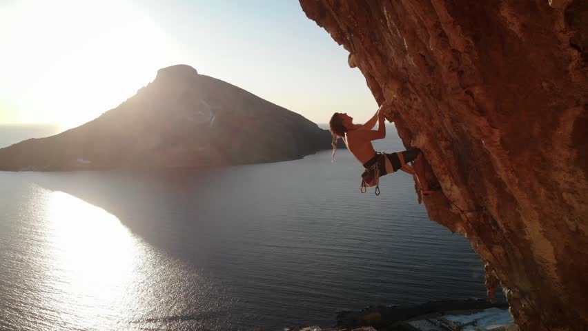 Climber climbing a hard and steep section of Grande Grotta cave at sunset and with Telendos island and coastline in the back at Kalymnos island, Greece. High quality 4k footage.