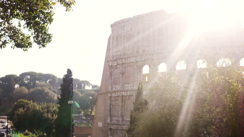 Beautiful young woman in colorful fashion riding bike in front of colosseum in Rome at sunset with trees attractive girl with straw hat close up shot steadycam