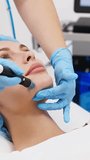 Vertical video. A cosmetologist in gloves performs vacuum cleaning and polishing of the skin of a young woman's face in a cosmetology clinic.
