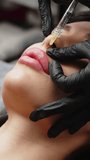 Vertical video. A surgeon wearing medical gloves carefully and slowly injects hyaluronic acid into a woman's lips using a syringe. lip augmentation procedure. beauty injections.