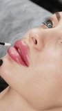 Vertical video. A cosmetologist touches a client's lips after injecting hyluaronic acid. Beauty injections on the lips. Beauty, injections and fashion.
