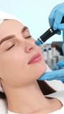 Vertical video. A cosmetologist performs vacuum cleaning and polishing of the skin of a young woman's face in a cosmetology clinic. Professional hardware procedures. Facial hydromassage process.
