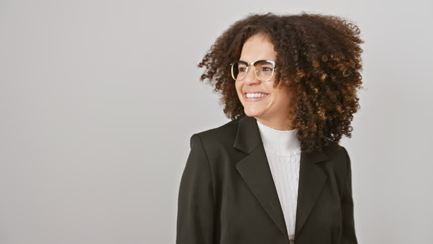 Confident curly-haired hispanic woman, radiating happiness and trust, stands laughing aside. her smile lights up her face, making her look naturally elegant. isolated against a white background.