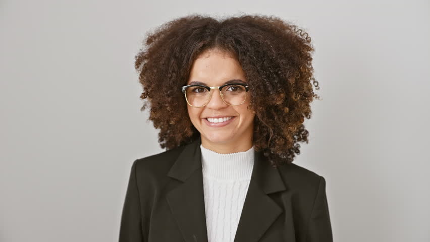 Attractive, curly-haired hispanic woman joyfully winks at the camera, standing against a seamless white wall. her cheerful face showing a sexy expression!