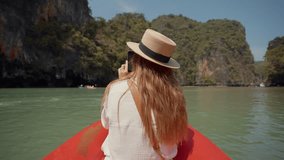 Woman sitting on boat passing lagoon. Back view female travel, riding on gondola, sitting on ship bow and looking take a photo of nature in a wicker hat in summer day. Adventure, travel lifestyle.
