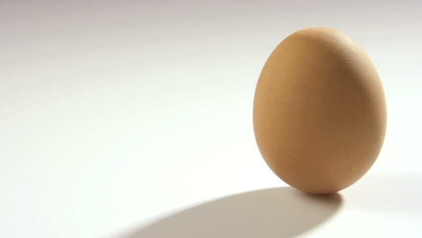 Brown egg rolling in slow motion on white table, 250 fps.