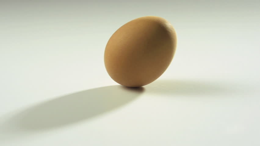 Brown egg rolling in slow motion on white table, 250 fps.