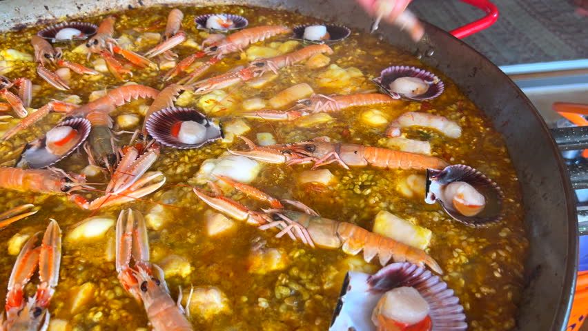 Cooking a huge traditional Spanish seafood Paella dish with shrimps, St Jacques scallops and Cigala Norway lobsters Nephrops norvegicus, delicious cooked rice with seafood, Marbella Spain, 4K shot