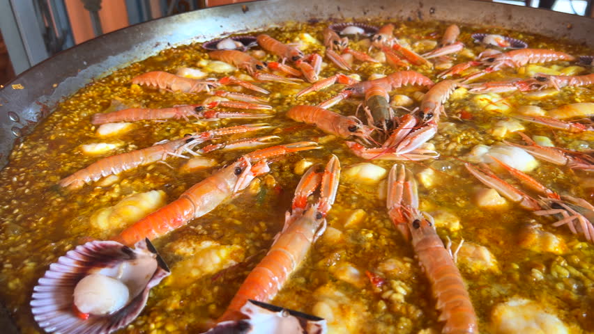 Cooking a big traditional Spanish seafood Paella dish with shrimps, St Jacques scallops and Cigala Norway lobsters Nephrops norvegicus, cooked rice with seafood, Marbella Spain, 4K shot