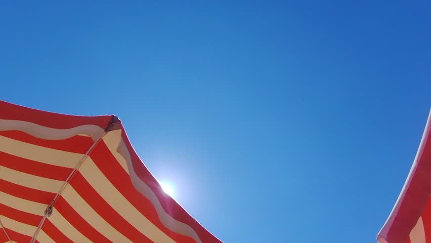 Summer time. Orange striped parasol under beautiful blue sky on background. 