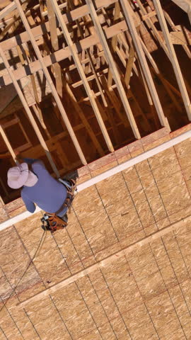 Building construction workers hammer nails into plywood on roof top of future home