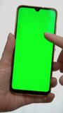 Hands of a person with a cell phone with green screen in his hand. Person scrolling a cell phone with green screen. Green screen on a cell phone. Green screen for advertising