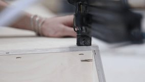 With the help of a pneumatic stapler, the craftsman joins plywood parts of furniture in production. Worker making sofa in furniture factory