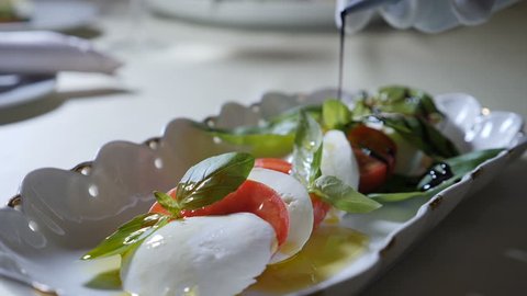 Healthy food and vegetarian concept. Close up of Pouring vinegar over caprese salad. Italian caprese salad with Mozzarella cheese. Slow motion