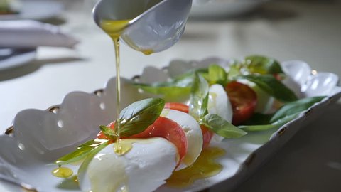 Healthy food and vegetarian concept. Close up of Pouring olive oil over caprese salad. Italian caprese salad with Mozzarella cheese. Slow motion