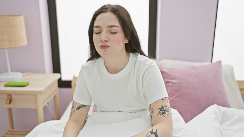 Terrified young woman in pyjamas sits on bedroom bed shouting in panic, hands expressing a fear-filled stop. shock and fear concept indoors.