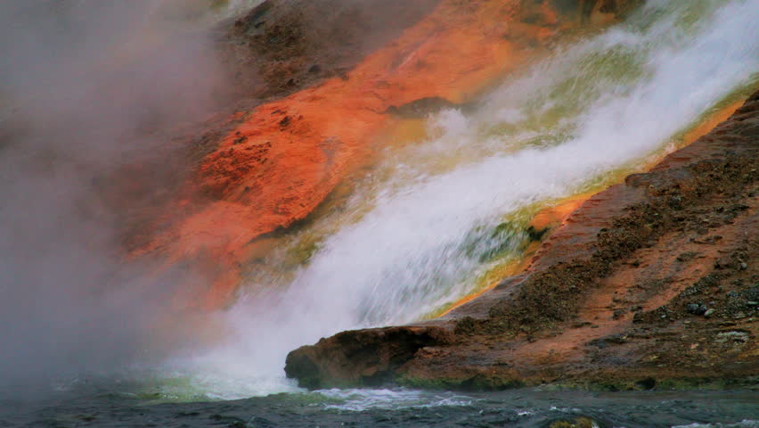 Impressive rapid waterfall making its way through unique orange soil, producing mist, falling into a stream with dark turbulent waters, Wyoming, Montana. High quality 4k footage