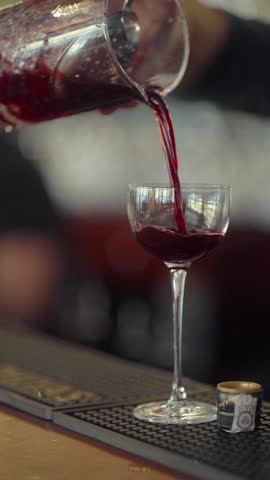 The bartender pours a chilled alcoholic cocktail into a glass through a julep strainer to separate the ice cubes. The cocktail flows in a beautiful stream into the glass. A drop falls into the glass.