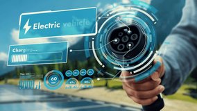 Focus EV charger pointing in front of camera display digital smart EV battery status hologram in blur nature and solar panel background. Electric charger and solar energy to reduce CO2 emission.Peruse - Powered by Shutterstock - Get 15% off with code: PIKWIZARD15