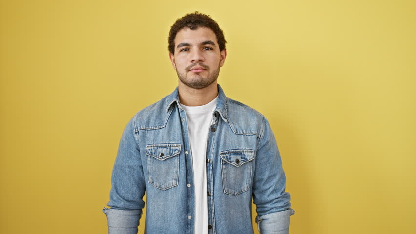 Pensive young arab man, serious expression etched on his face, hand thoughtfully on chin, standing isolated on a yellow background, contemplating a confusing idea with concentrated doubt.