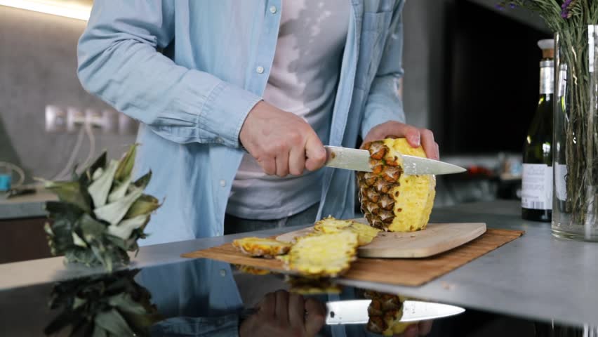 Man cut pulp of peeled ripe pineapple in kitchen, sweet delicious yellow pineapple cut into pieces.