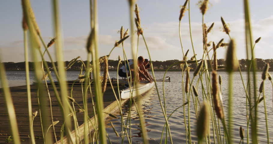 Side view of four Caucasian male rowers, standing in a row on a jetty, holding a boat, taking it out of the water, during a sunset, in slow motion