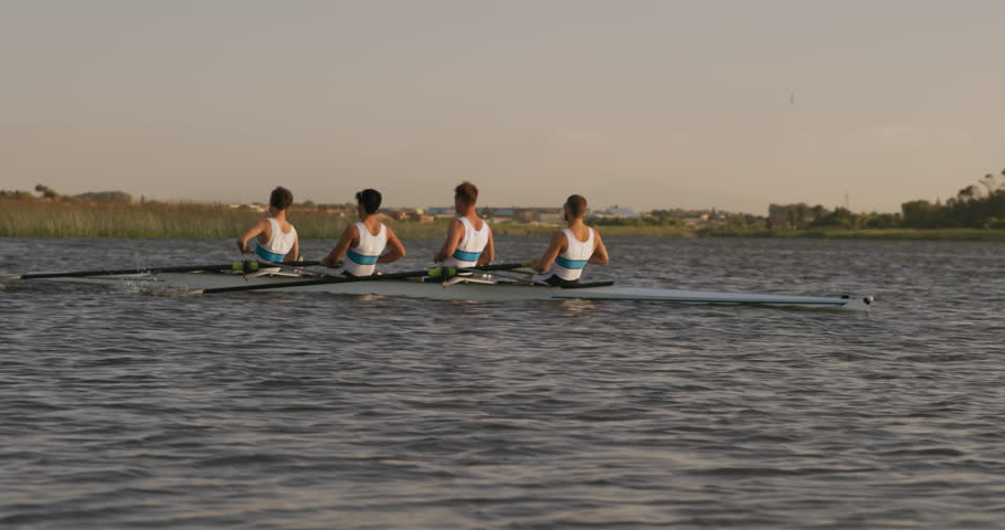 Side view of four Caucasian male rowers, during a rowing practice, sitting in a boat, rowing, during a sunset, in slow motion