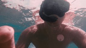 A caucasian man in an underwater swimming mask films himself on an action camera. A man takes a selfie video while swimming underwater. 
