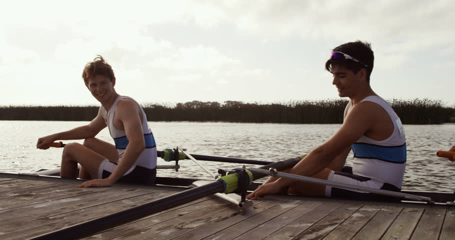 Side view of three Caucasian male rowers, after a rowing practise, sitting in a boat by a jetty, talking and discussing, on a sunny day, in slow motion